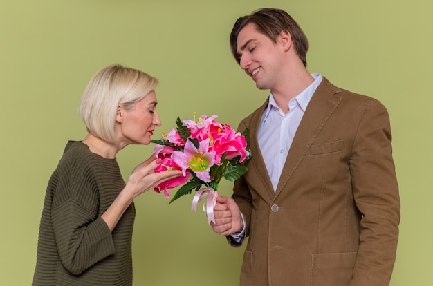 Jovem casal lindo feliz dando um buquê de flores para a namorada, comemorando o dia internacional da mulher em pé sobre a parede verde