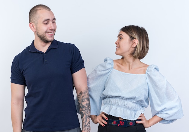 Jovem casal lindo homem e mulher felizes e positivos olhando um para o outro sorrindo alegremente em pé