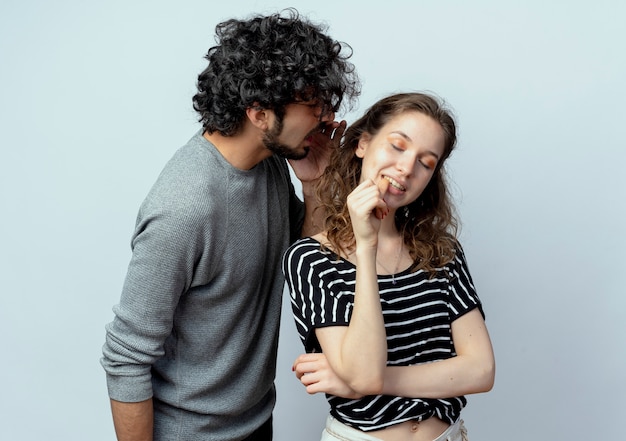 Jovem casal lindo, homem e mulher, homem sussurrando um segredo ou uma fofoca interessante para a namorada, sobre fundo branco