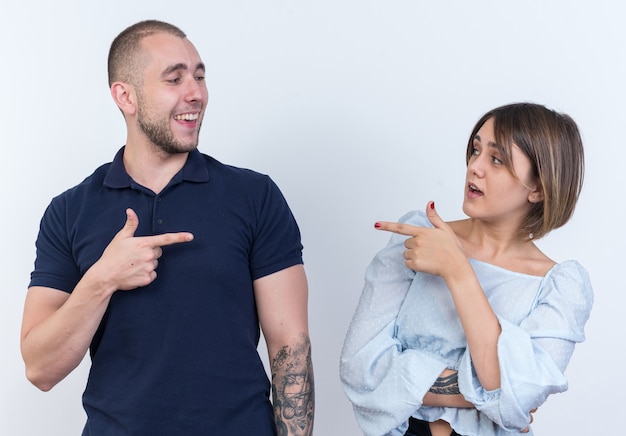 Jovem casal lindo homem e mulher olhando um para o outro, apontando com o dedo indicador um para o outro, sorrindo, feliz e positivo em pé