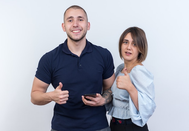 Jovem casal lindo, homem e mulher, parecendo feliz e positivo, sorrindo alegremente, mostrando os polegares em pé