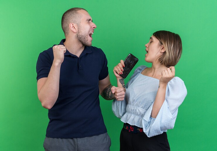 Foto grátis jovem casal lindo homem e mulher segurando o smartphone com os punhos cerrados, feliz e animado, regozijando-se com o sucesso em pé