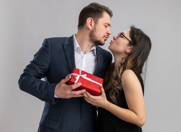 Jovem casal lindo homem e mulher segurando um presente e indo se beijar, feliz no amor, comemorando o dia dos namorados