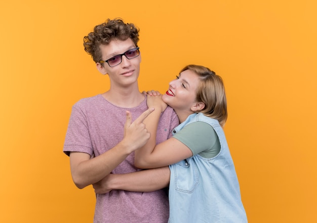 Jovem casal lindo homem e mulher vestindo roupas casuais felizes e apaixonados em pé juntos, sorrindo sobre a parede laranja