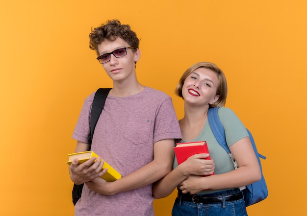 Foto grátis jovem casal lindo homem e mulher vestindo roupas casuais segurando livros sorrindo em pé sobre uma parede laranja