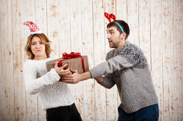 Jovem casal lindo lutando pelo presente de Natal sobre a superfície de madeira