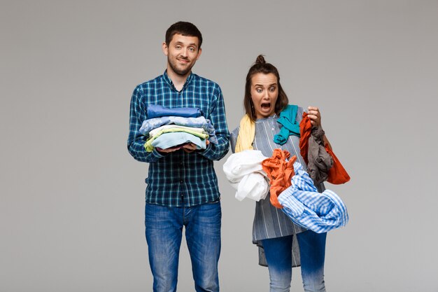 Jovem casal lindo segurando lavar roupas sobre parede cinza