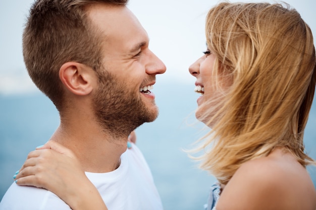 Jovem casal lindo sorrindo, regozijando-se, vista para o mar.