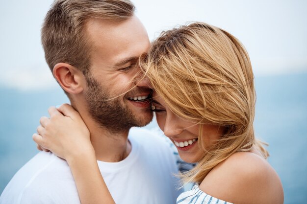 Jovem casal lindo sorrindo, regozijando-se, vista para o mar.