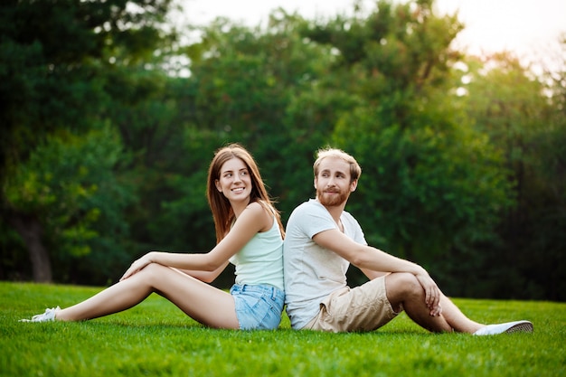 Jovem casal lindo sorrindo, sentado na grama no parque.