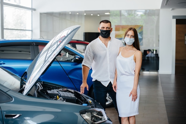 Jovem casal mascarado escolhe um novo veículo e consulta um representante da concessionária no período da pandemia. venda de carros e vida durante a pandemia.