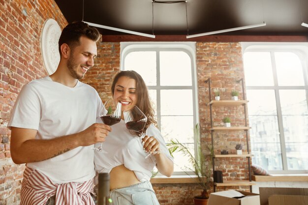 Jovem casal mudou-se para uma nova casa ou apartamento. beber vinho tinto, transportar e relaxar após limpar e desembalar. pareça feliz e confiante. família, mudança, relações, primeiro conceito de casa.