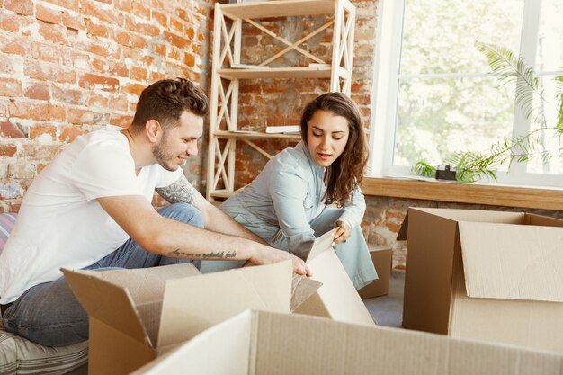 Jovem casal mudou-se para uma nova casa ou apartamento. Desempacotando caixas de papelão juntos, se divertindo no dia da mudança