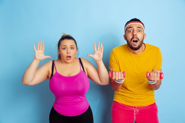 Jovem casal muito caucasiano com roupas brilhantes, treinando no espaço azul. Conceito de esporte, emoções humanas, expressão, estilo de vida saudável, relação, família