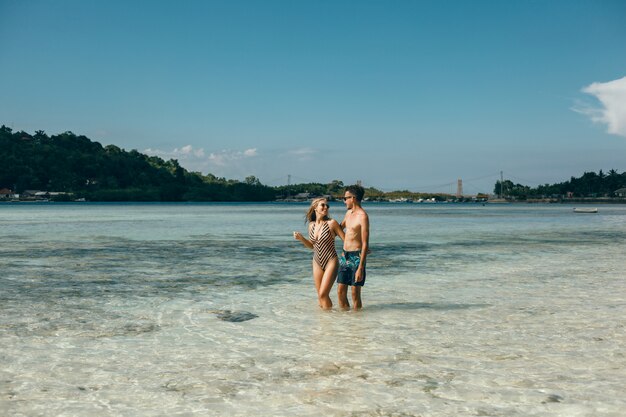 jovem casal posando na praia, se divertindo no mar, rindo e sorrindo