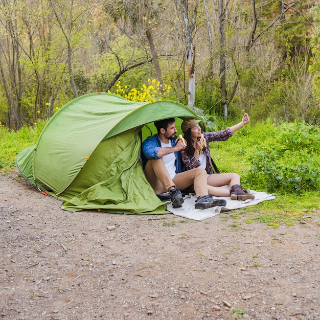 Foto grátis jovem casal posando para selfie perto da tenda