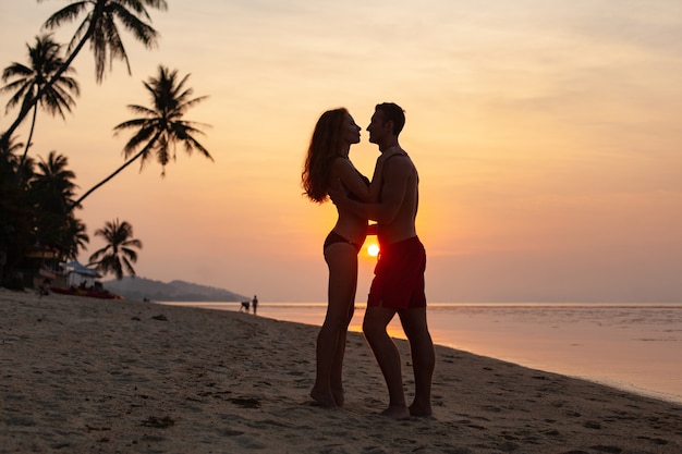 Jovem casal romântico apaixonado no pôr do sol feliz na praia de verão juntos se divertindo usando maiôs