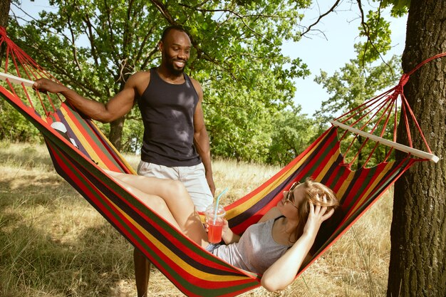 Jovem casal romântico internacional multiétnico ao ar livre no Prado em um dia ensolarado de verão. Homem afro-americano e mulher caucasiana fazendo piquenique juntos. Conceito de relacionamento, verão.