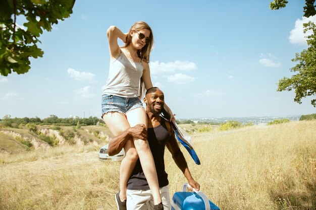 Jovem casal romântico internacional multiétnico ao ar livre no Prado em um dia ensolarado de verão. Homem afro-americano e mulher caucasiana fazendo piquenique juntos. Conceito de relacionamento, verão.