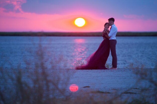 Jovem casal romântico relaxante na praia, assistindo o pôr do sol