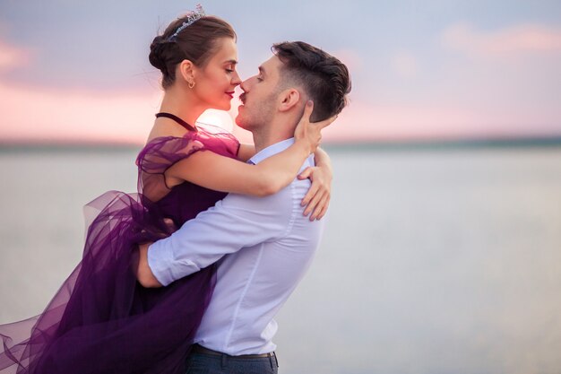 Jovem casal romântico relaxante na praia, assistindo o pôr do sol