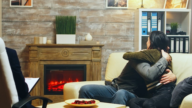 Jovem casal se abraça sentado no sofá na terapia depois de falar sobre suas dificuldades.