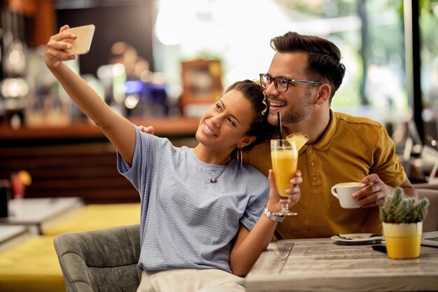 Jovem casal se divertindo enquanto toma selfie com celular em um bar