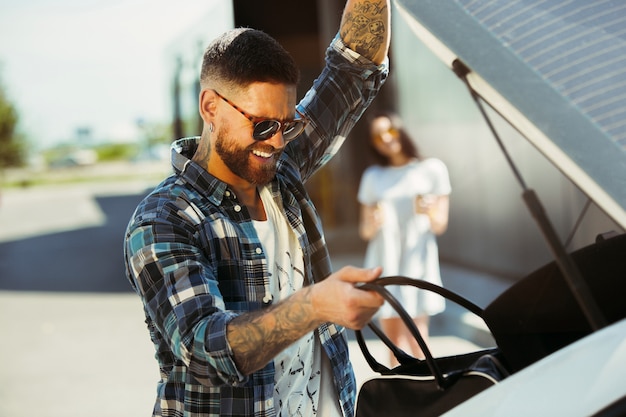 Foto grátis jovem casal se preparando para a viagem de férias no carro em um dia ensolarado. mulher e homem às compras e pronto para ir para o mar, ribeirinha ou oceano. conceito de relacionamento, férias, verão, feriado, fim de semana.