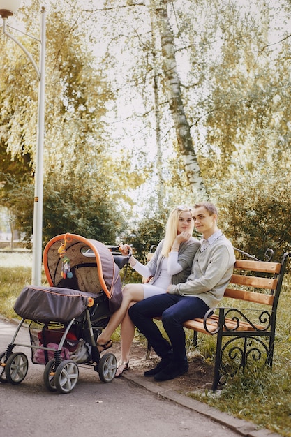 Jovem casal sentado em um banco em um parque com um carrinho de bebê ao lado