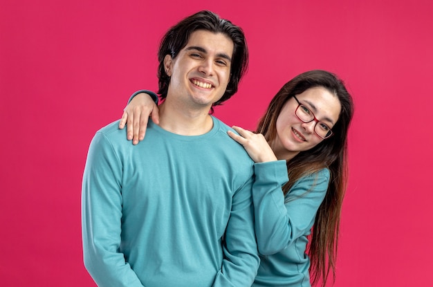 Jovem casal sorridente no dia dos namorados abraçando um cara sorridente isolado no fundo rosa