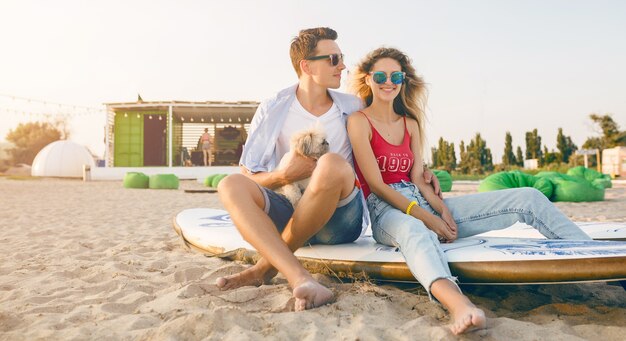 Jovem casal sorridente se divertindo na praia brincando com cachorros da raça shih-tsu