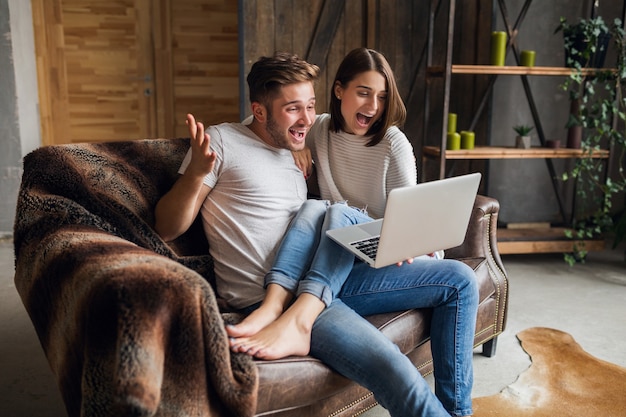 Jovem casal sorridente sentado no sofá em casa com roupa casual