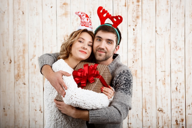 Jovem casal sorrindo abraçando segurando o presente de natal sobre a superfície de madeira