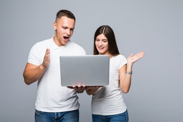 Jovem casal surpreso em camiseta branca assistindo algo no laptop da marca