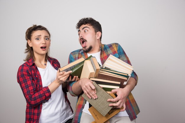 Jovem casal tentando segurar vários livros na parede cinza