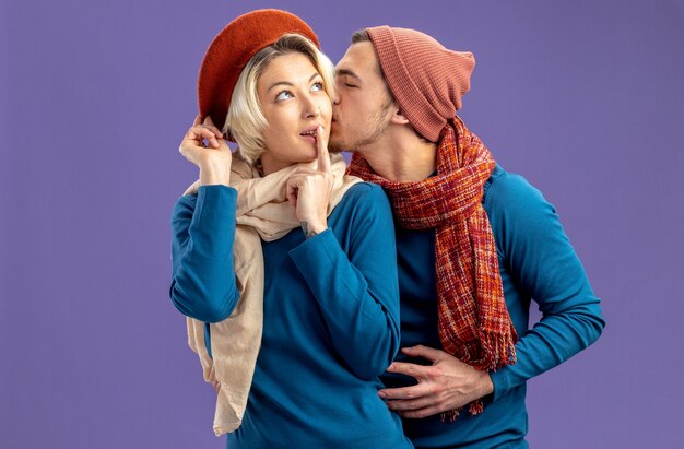 Jovem casal usando chapéu com lenço no dia dos namorados, beijando a bochecha da garota isolada no fundo azul