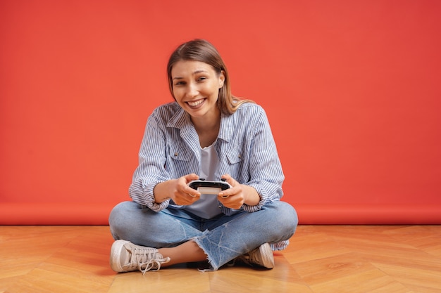 Jovem casual animada jogando videogame se divertindo no vermelho