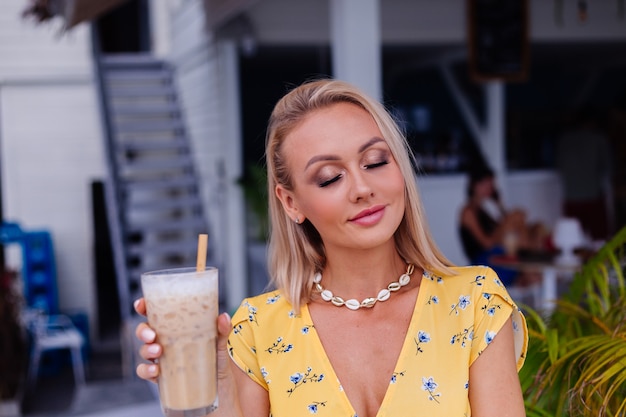 Jovem caucasiana, calma, bonita, feliz, com maquiagem brilhante para a noite, usando um vestido amarelo de verão e um colar de conchas do mar