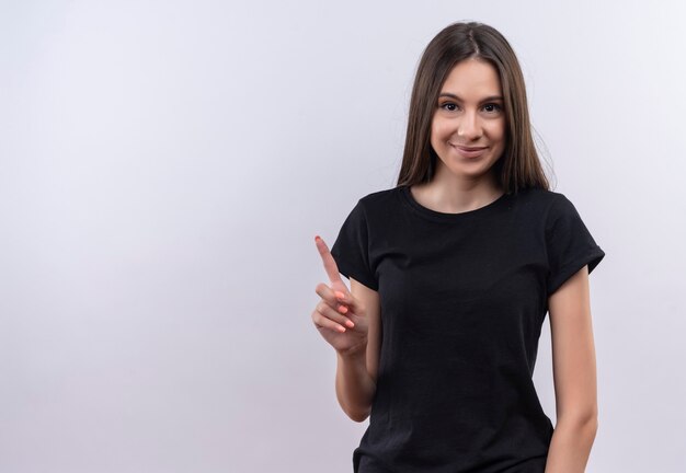 jovem caucasiana satisfeita vestindo camiseta preta apontando o dedo para cima na parede branca isolada