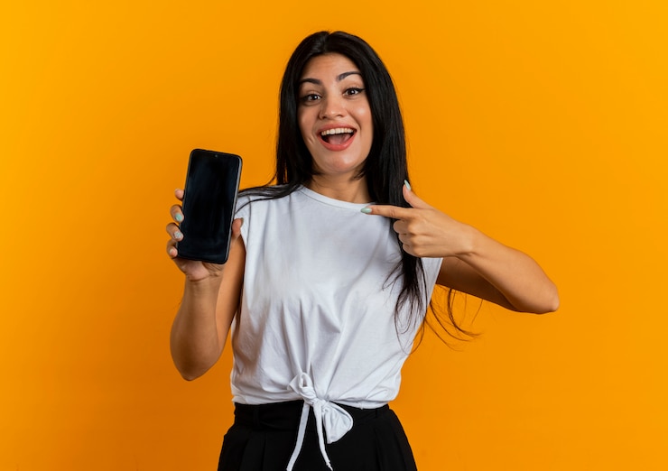 Foto grátis jovem caucasiana surpreendida segurando e apontando para o telefone
