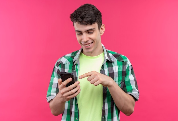 Foto grátis jovem caucasiano sorridente, vestindo uma camisa verde, discar o número do telefone em fundo rosa isolado