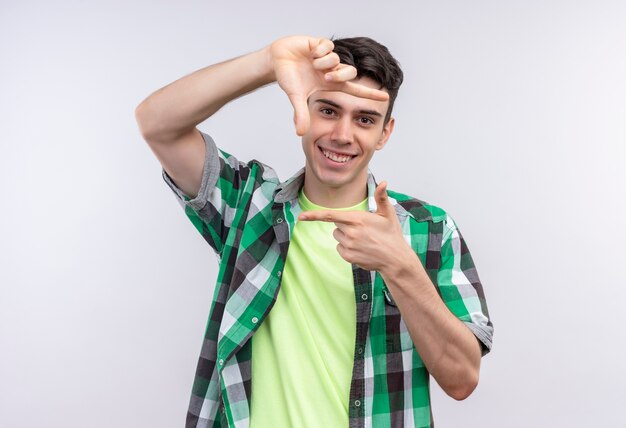 Jovem caucasiano sorridente, vestindo uma camisa verde, mostrando um gesto de foto em fundo branco