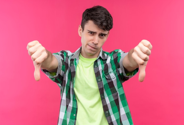 Foto grátis jovem caucasiano triste vestindo uma camisa verde com os polegares para baixo em fundo rosa isolado