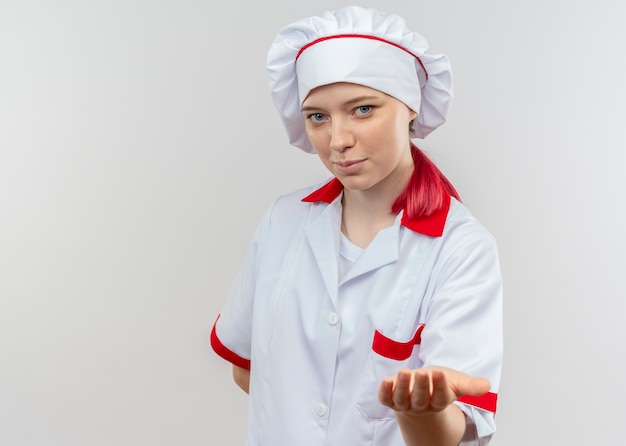 Jovem chef feminina loira satisfeita com uniforme de chef segurando a mão isolada na parede branca