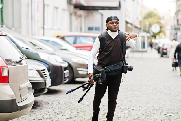 Jovem cinegrafista afro-americano profissional segurando uma câmera profissional com equipamento tripé Pro cinegrafista afro vestindo duraq preto fazendo vídeos