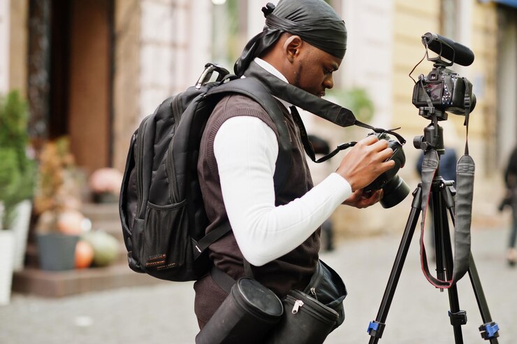Foto grátis jovem cinegrafista afro-americano profissional segurando uma câmera profissional com equipamento tripé pro cinegrafista afro vestindo duraq preto fazendo vídeos