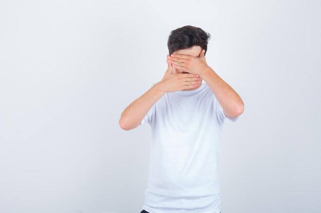 Jovem cobrindo o rosto com as mãos na camiseta e parecendo sensato