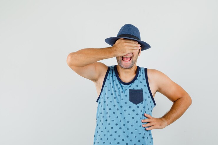 Foto grátis jovem cobrindo os olhos com a mão na camiseta azul, chapéu e parecendo animado