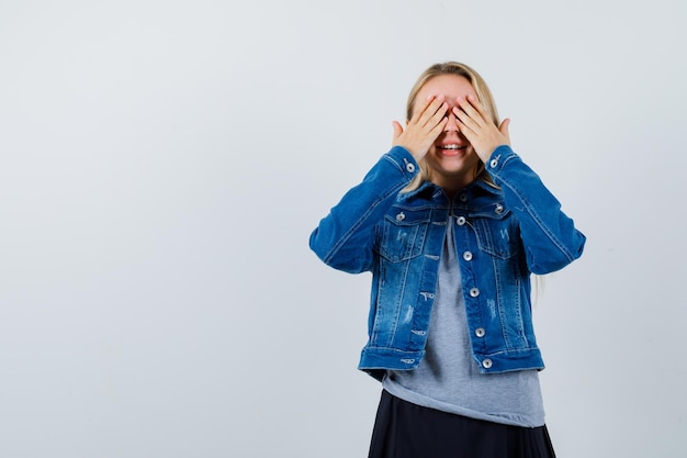 Jovem, cobrindo os olhos com as mãos na camiseta, jaqueta jeans, saia e linda.