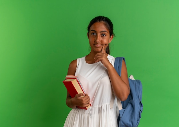 jovem colegial usando mochila segurando livro com caderno colocando o dedo na bochecha